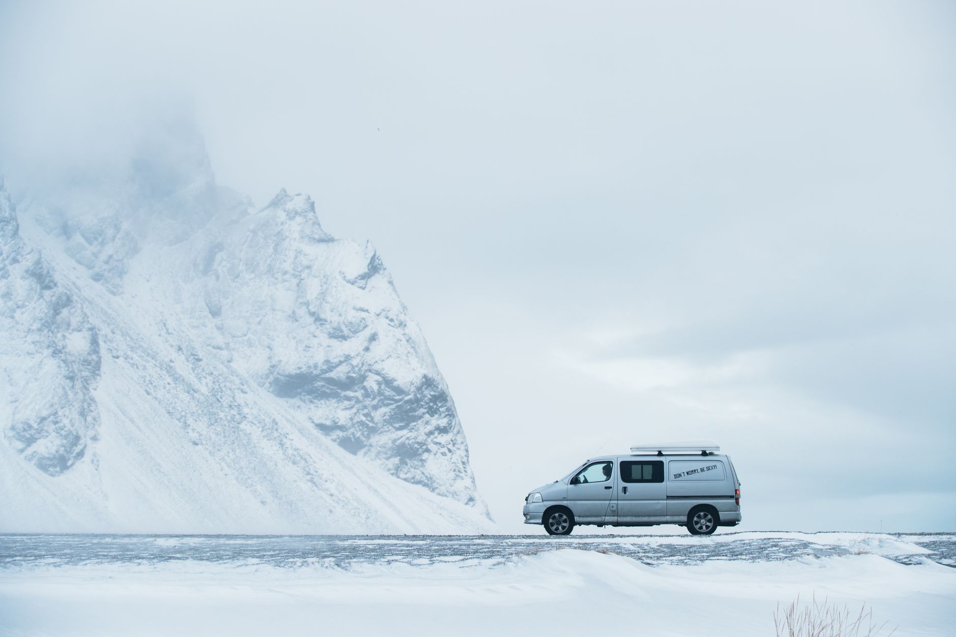 A van traverses the snowy roads of Iceland near towering icy mountains, capturing the spirit of winter adventure.