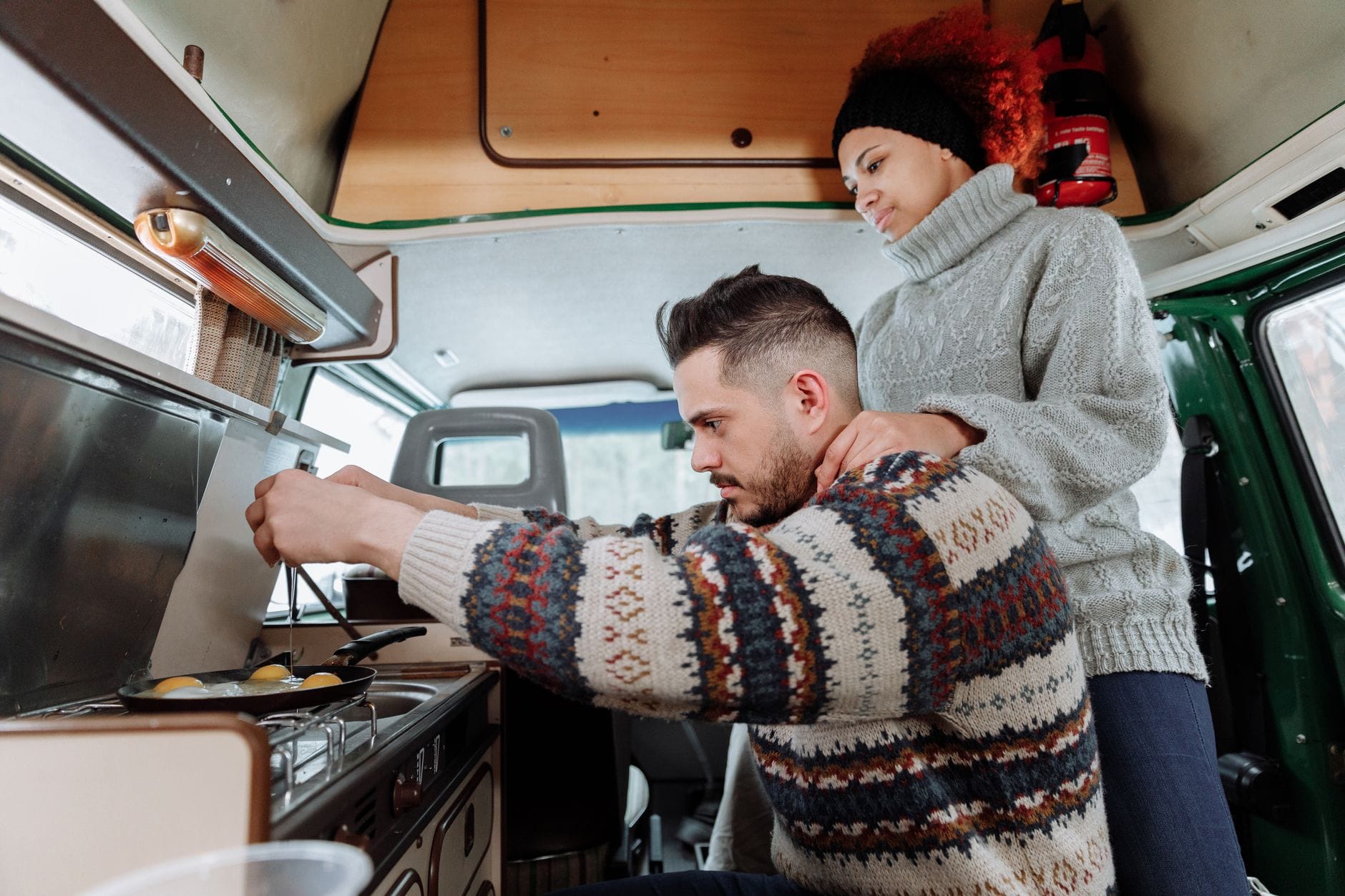 Interracial couple cooking breakfast in cozy camper van during a road trip adventure.