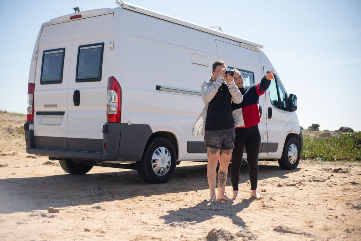 Pareja de viaje junto a una furgoneta camper compacta en un paisaje desértico